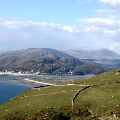 a view of a field with a lake and mountains at Cosy modern cottage by the sea, heart of snowdonia in Llwyngwril