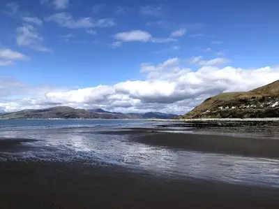 a beach with the ocean and mountains in the background at Cosy modern cottage by the sea, heart of snowdonia in Llwyngwril