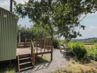 a wooden deck sitting next to a green building at Aston - Shepherd Hut in Craven Arms