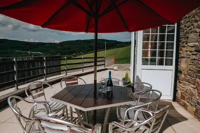 a table and chairs with an umbrella on a balcony at Luxury 5-Bed Farmhouse - Sleeps 8 & Hot Tub in Brecon