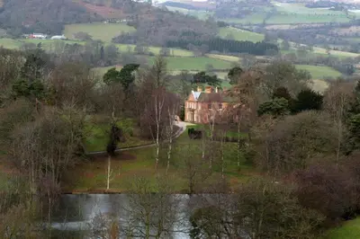 a large house on a hill next to a body of water at The Coach House at Bryngwyn Hall in Llanfyllin