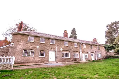 an old brick building with a white door on a grass field at Garden House in North Lydbury