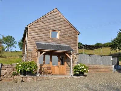 a small wooden house with a porch and some flowers at Rockhill Farm Hay Barn in Craven Arms