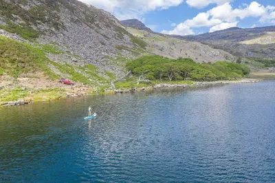 a person is standing on a paddle board in a lake at Ty-Newydd-Frongaled in Dyffryn