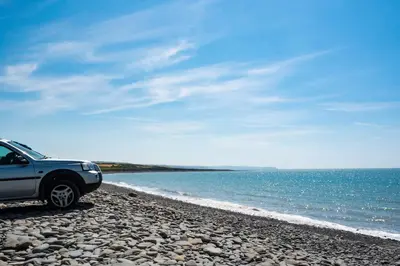 a car parked on a rocky beach near the water at Tan Y Bryn in Llanrhystyd