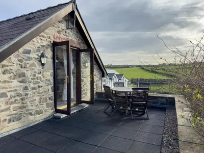 a stone cottage with a table and chairs on a patio at Crogal Stable in New Quay