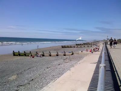 a beach with people walking and people on the beach at Trem Y Mor - Edge of the Sea in Tywyn