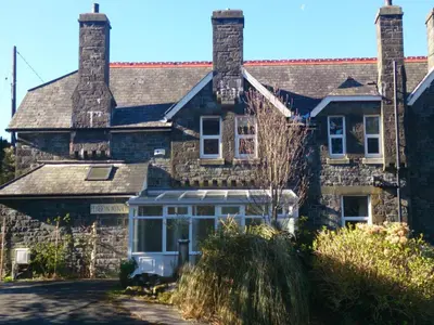 an old stone house with a greenhouse in front of it at Penbryn Mynach Holiday Cottage in Barmouth