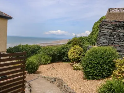 a garden with a stone wall and the ocean at Morolwg in Barmouth