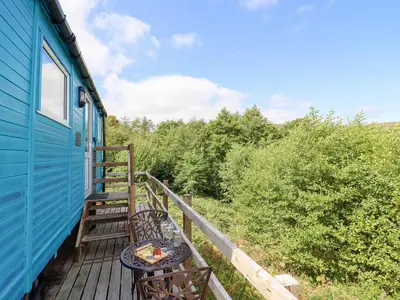 a deck with a table and chairs on a blue house at Cuckoo at Wild Valley Huts in Oswestry