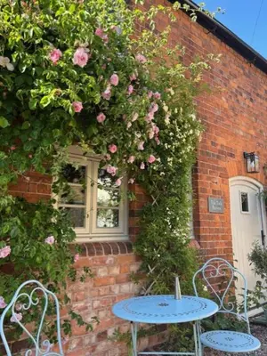 two tables and chairs in front of a brick building with roses at The Old Rectory Tack Rooms in Shrewsbury
