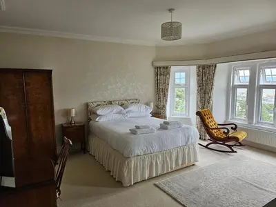 a bedroom with a bed and a chair and windows at Y Garth, Sleeps 12 in Barmouth