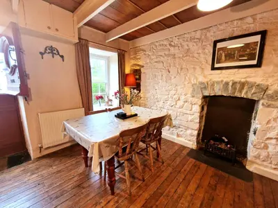 a dining room with a stone fireplace and a wooden table at Arwel Llangrannog in Llanllwchaiarn