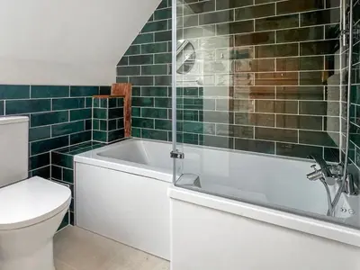 a bathroom with a tub and a toilet and green tiles at Uk46578 - Drifthouse in Church Stretton