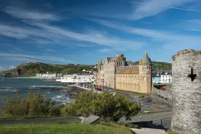 an old building with a tower next to the water at Plas Hafan Apartment 2 Aberystwyth in Aberystwyth