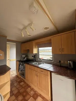 a kitchen with wooden cabinets and a sink and a window at Spacious 2 bedroomed mobile home in Aberystwyth