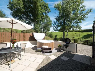 a patio with a table and an umbrella and a grill at Briallen Aberystwyth in Llanrhystyd