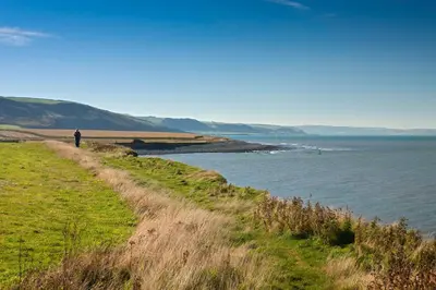 a person walking along a path next to a body of water at Briallen Aberystwyth in Llanrhystyd