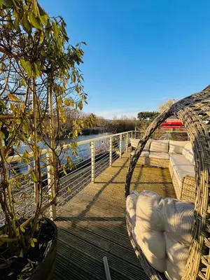 a hammock on a deck next to the water at By the River in Glasbury