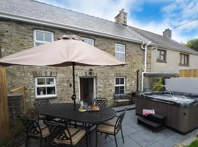 a patio with a table with an umbrella and a hot tub at Bryndalis Aberaeron in Ciliau-Aeron