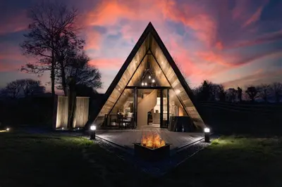a triangular house with a fire in the yard at night at The Tri-Pod in Llanarth