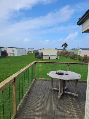 a picnic table on a deck with a field at Cosy caravan Sunbeach in Llwyngwril