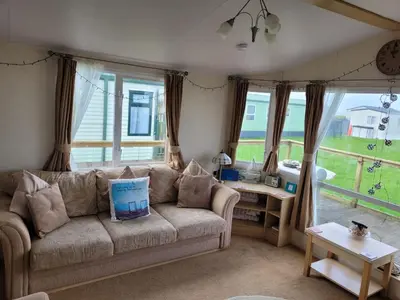 a living room with a couch and a table and windows at Cosy caravan Sunbeach in Llwyngwril