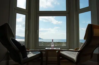 a window with two chairs and a bottle on a table at Abermaw Sea View Apartment in Barmouth