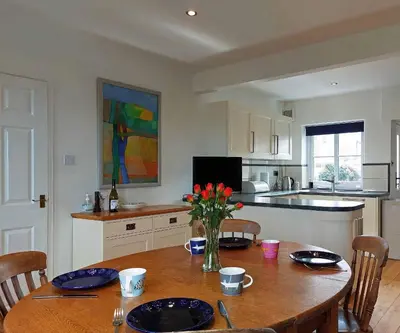 a kitchen with a wooden table with a vase of flowers at Garreg Wen - White Stone, family holiday home in Barmouth