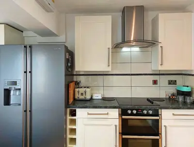 a kitchen with white cabinets and a stainless steel refrigerator at Garreg Wen - White Stone, family holiday home in Barmouth