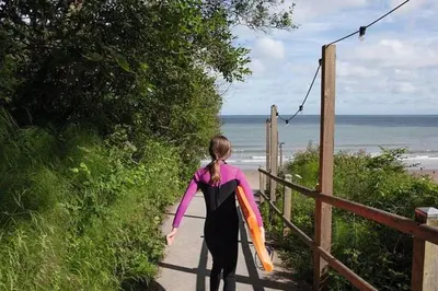 a woman walking down a path with a surfboard at HARRIES LODGE QUAY WEST milkwood way in New Quay