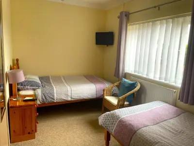 a bedroom with two beds and a chair and a window at Caerhafod Llangrannog in Llanllwchaiarn