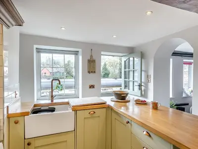a kitchen with a wooden counter top and two windows at Dee Bank Cottage in Llangollen