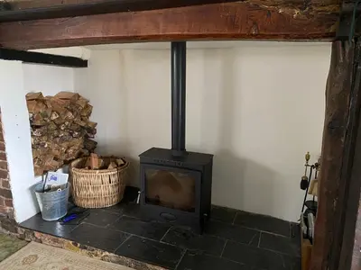 a wood stove in a room with a basket of logs at Bryntirion Farmhouse Rooms (with bathroom) in Llanfair Caereinion