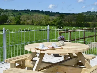 a wooden picnic table on a patio with a fence at Cob Cottage in Tregaron