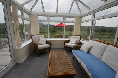 a conservatory with a couch and chairs and windows at Cob Cottage in Tregaron