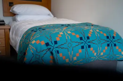 a bed with a blue and orange blanket on it at Gwesty Cymru in Aberystwyth