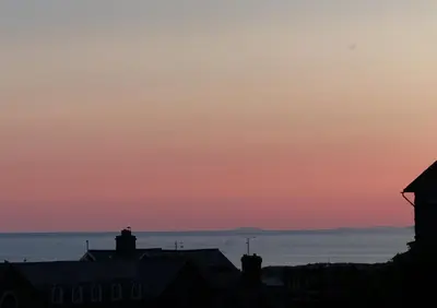 a sunset over the ocean with houses in the foreground at 2-Bedroom cottage in Barmouth old town with sea views in Barmouth