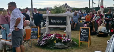 a crowd of people standing around a sign with flowers at The Springfield Hotel in Fairbourne