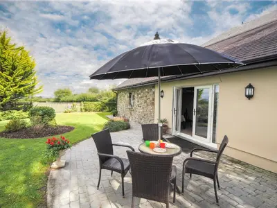 a patio with a table and chairs and an umbrella at Nyth y Wennol Aberaeron in Llanarth