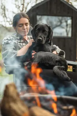 a woman holding a dog sitting next to a fire at Cyra in Llangollen