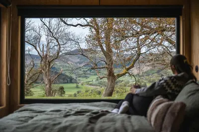 a woman sitting on a bed looking out of a window at Cyra in Llangollen
