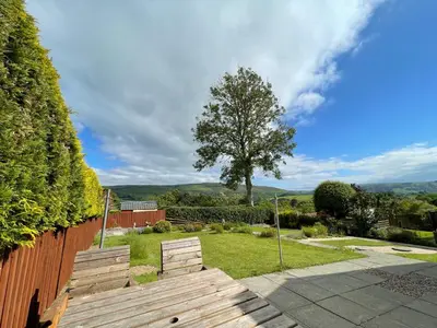 a wooden bench in a yard with a tree at Ty Ray Penmaes in Rhayader