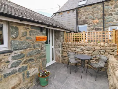 a stone house with a table and chairs on a patio at Y Stabl in Dyffryn