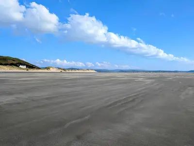 an empty beach with a blue sky and clouds at Pencartref Apartment - 4 Bedrooms, 3 Bathrooms, Sleeps 7-8 in Aberdyfi