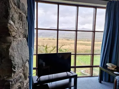 a living room with a large window with a chair and a television at Swn y nant Barmouth road A496 Llanelltyd in Penmaenpool