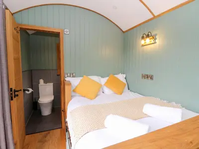 a bedroom with a bed with yellow pillows and a toilet at Dam View Shepherds Hut in Rhayader