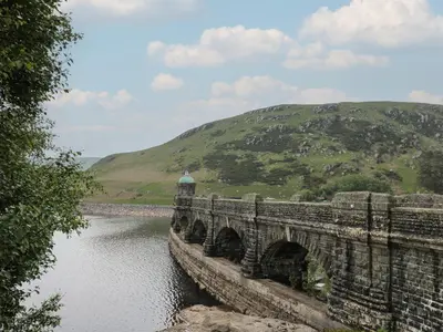 a bridge over a river with a hill in the background at Osborne House in Rhayader
