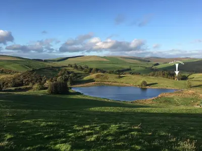 a lake in the middle of a green field with a windmill at Llynhillyn Cottage in Presteigne