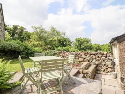 a table and chairs on a patio with a stone wall at Ivy Cottage in Harlech